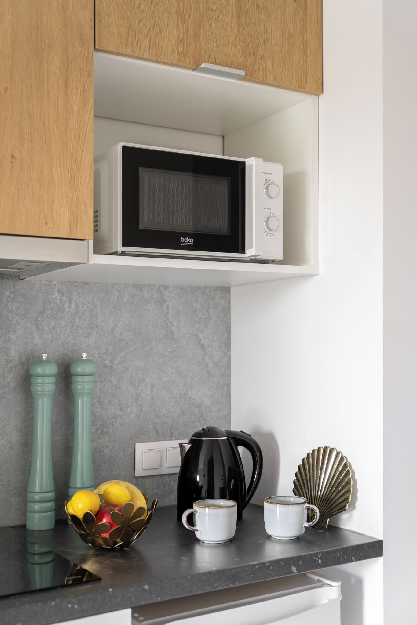 A kitchen with a microwave, a kettle, and a bowl of fruit on the counter.