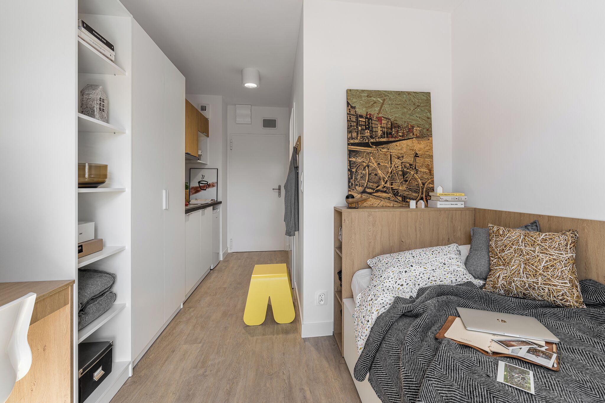 A modern bedroom with a bed, a painting, and a small stool.