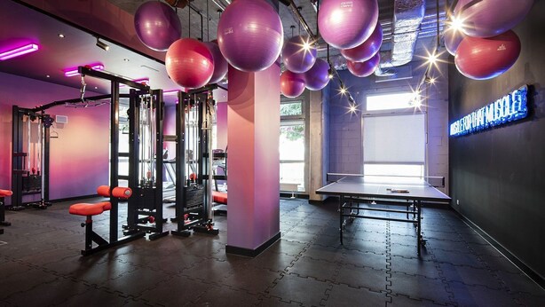 Un gimnasio con equipo de ejercicio, una mesa de ping pong y un letrero de neón.