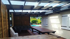 Un patio al aire libre con una mesa de madera, bancos y una piscina al fondo.