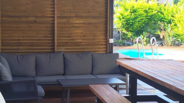 Una terraza de madera con piscina, un sofá gris y una mesa de madera.