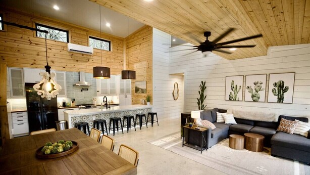 A modern kitchen with white cabinets, a central island, and a dining area with a wooden table and chairs. - Shangri-La, a spacious retreat at Wanderin’ Star Farms (Dripping Springs)