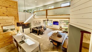 A spacious loft-style living area with a kitchen, dining table, and a staircase leading to an upper level. - Shangri-La, a spacious retreat at Wanderin’ Star Farms (Dripping Springs)