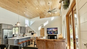 A modern kitchen with a central island, bar stools, and a large flat-screen TV mounted on the wall.