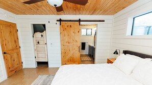 A bedroom with a large bed, wooden walls, a ceiling fan, and a sliding barn door.