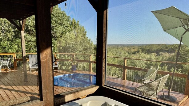 A hot tub with a wooden deck and outdoor seating, overlooking a forested area.