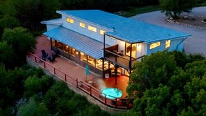 A modern house with a large deck, a hot tub, and a view of the surrounding forest.