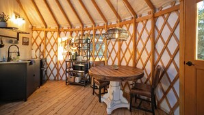 Um interior acolhedor com uma mesa e cadeiras de madeira, uma área de cozinha com pia e eletrodomésticos, e um design de parede com treliça.
