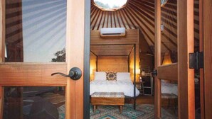 A cozy, wooden interior with a bed, a small bench, and a window with a view. - Yurt in the trees w TX stars & Pickleball (Dripping Springs)