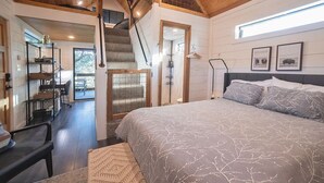 A bedroom with a large bed, a staircase, and a view of the outdoors. - Cozy Cabin w a view & Tesla EV Charger (Dripping Springs)
