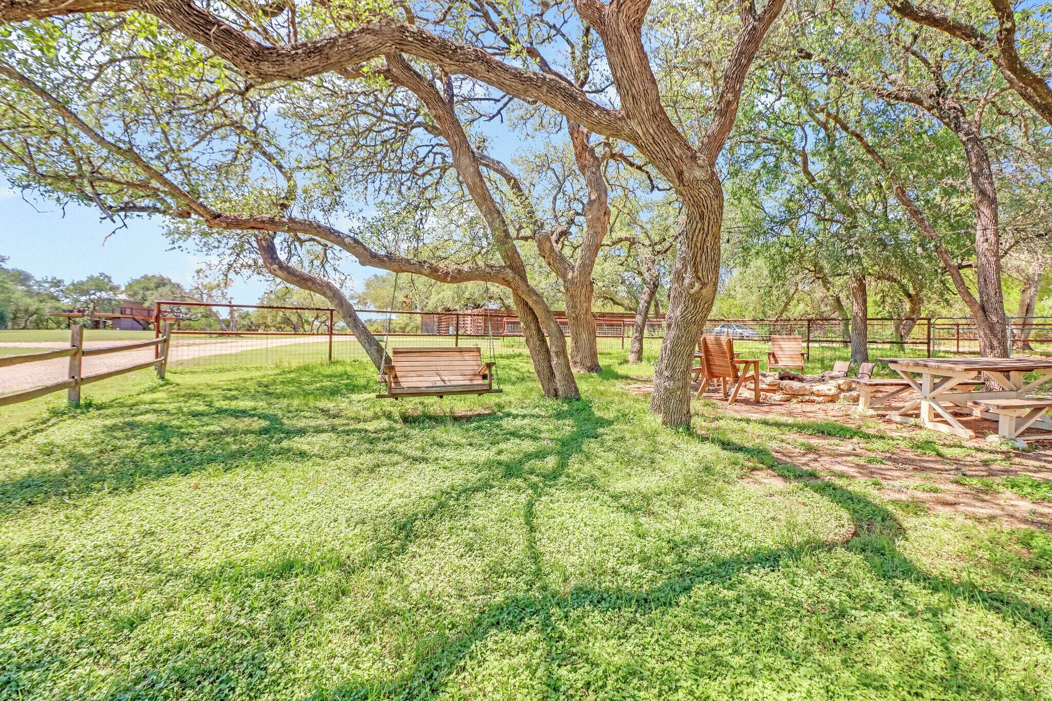 A park with a wooden swing, picnic tables, and a fenced area.