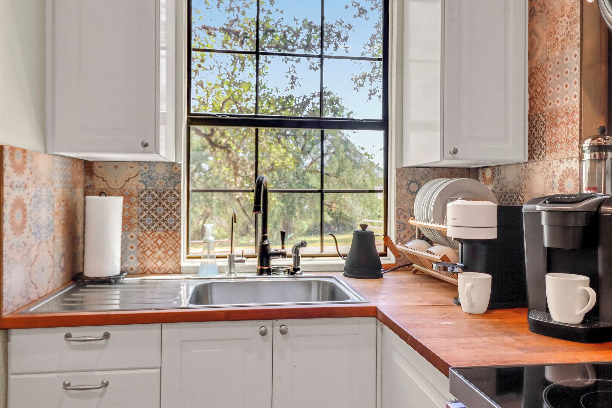 A kitchen with a sink, coffee maker, and window with a view of trees.