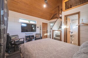 A bedroom with a bed, a TV, a desk, and a chair. - Keep it Cozy, a secluded tiny home at Wanderin’ Star Farms (Dripping Springs)