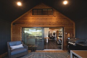A cozy cabin interior with a wooden exterior, a glass door leading to a dining area, a comfortable seating area, and a barbecue grill. - Keep it Cozy, a secluded tiny home at Wanderin’ Star Farms (Dripping Springs)