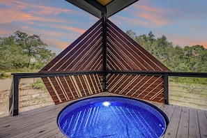 A hot tub on a wooden deck with a view of trees and a sunset sky. - Driftwood ↠ Hill Country cabin w Loft & Light & Pickleball (Dripping Springs)