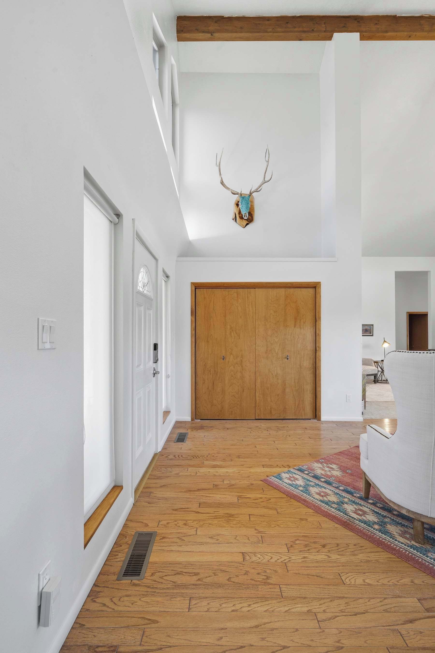 Un pasillo amplio con suelo de madera, una puerta de madera grande y una cornamenta de venado montada en la pared.