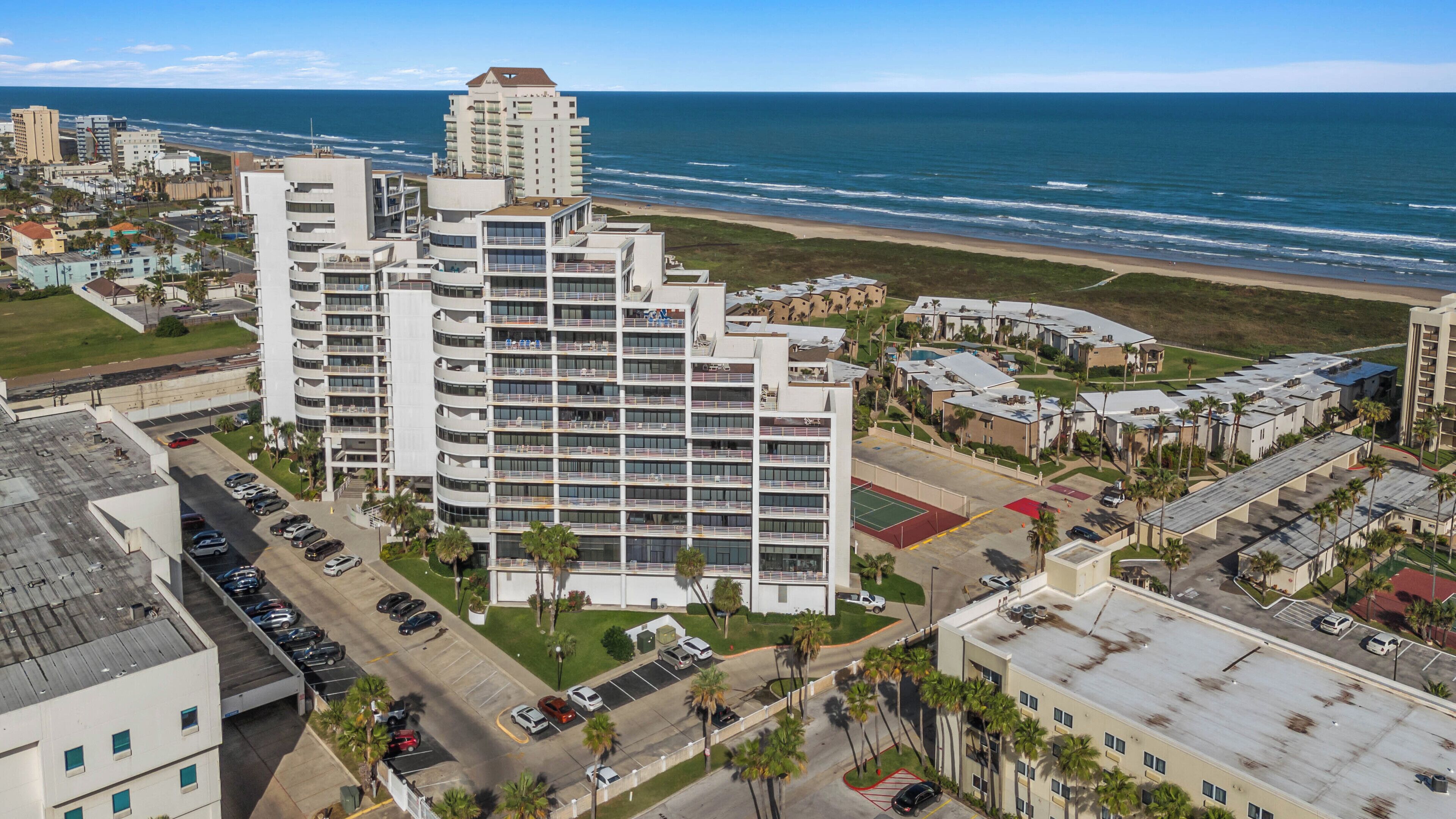 Um hotel alto com vários andares, estacionamento e vista para a praia e oceano.