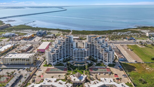 Un hotel moderno con un cortile centrale, diversi piani e vista sul mare e un ponte sullo sfondo.