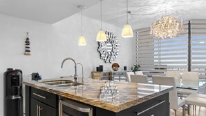 Una cucina moderna con un piano di lavoro in granito, elettrodomestici in acciaio inossidabile, illuminazione a sospensione e uno specchio decorativo.