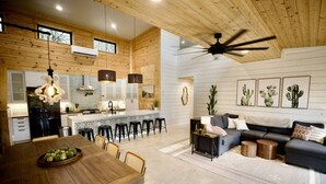A spacious living area with a dining table, sofa, and a kitchen in the background. - Whole Ranch Buyout for your team or family! (Dripping Springs)