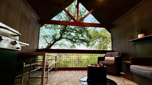 A cozy room with a large window, a fireplace, and a dining area. - Whole Ranch Buyout for your team or family! (Dripping Springs)