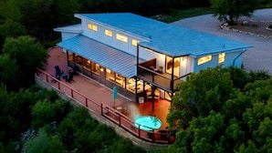 A modern house with a large deck, a hot tub, and a view of the surrounding forest. - Whole Ranch Buyout for your team or family! (Dripping Springs)