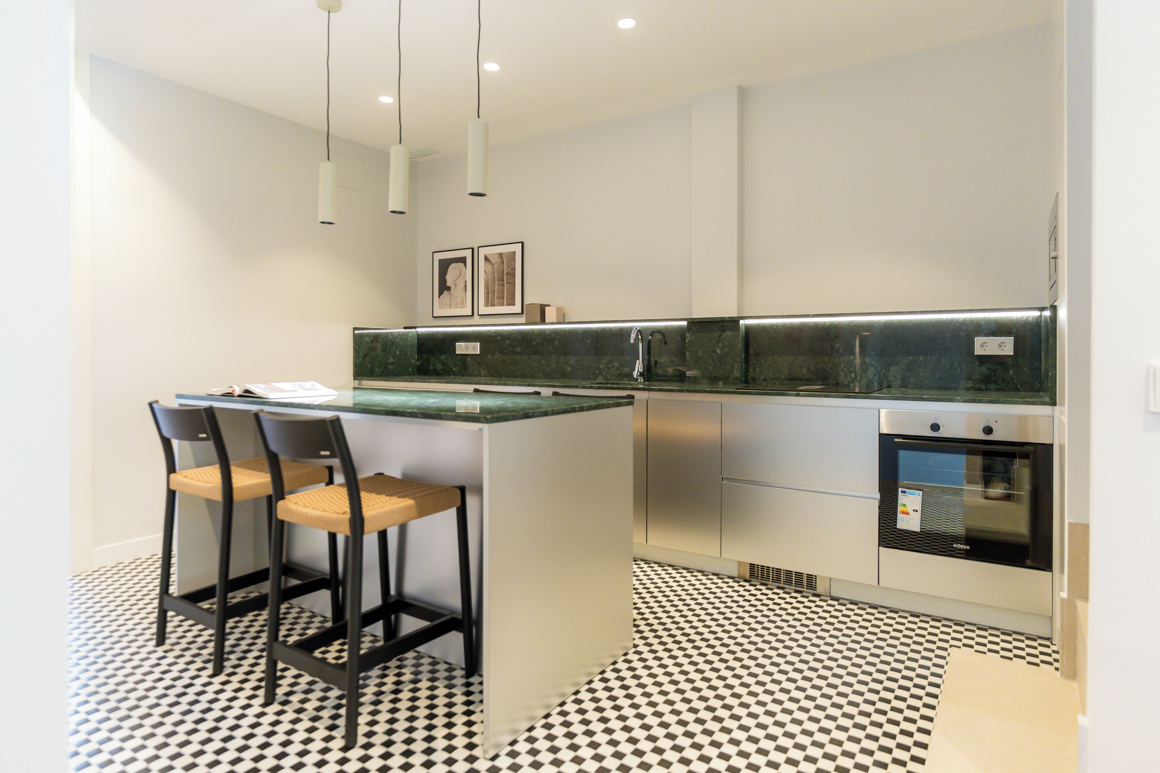 Una cucina moderna con isola centrale, sgabelli da bar, forno integrato e pavimento decorato.