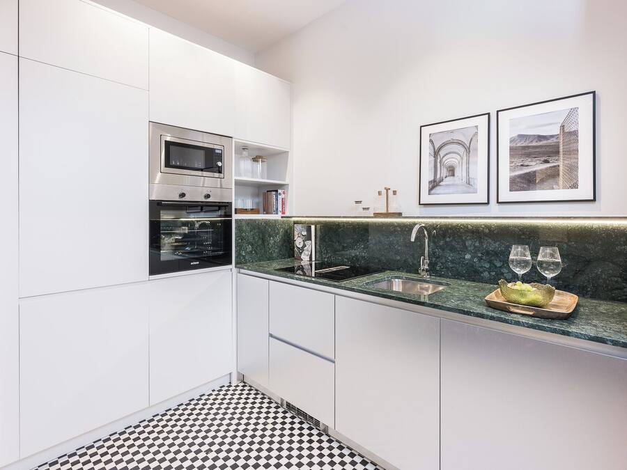 Een moderne keuken met witte kastjes, een zwart-wit geruite vloer, een ingebouwde oven, een gootsteen met een marmeren aanrechtblad en twee ingelijste foto's aan de muur.