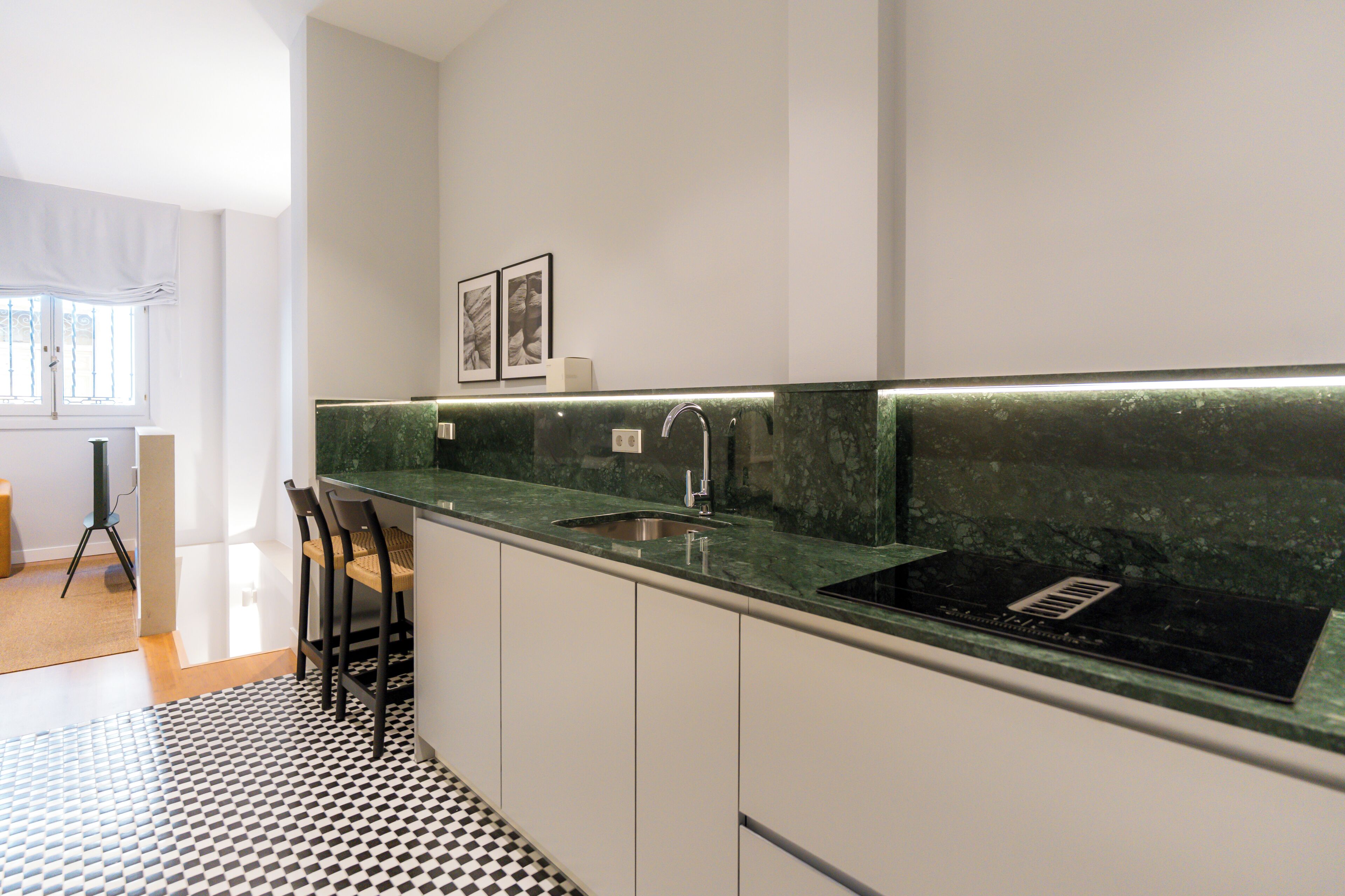 A modern kitchen with a black and white checkered floor, a green marble countertop, and a stainless steel sink.