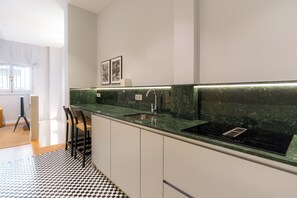 Una cocina moderna con piso a cuadros blanco y negro, encimera de mármol verde y pileta de acero inoxidable.