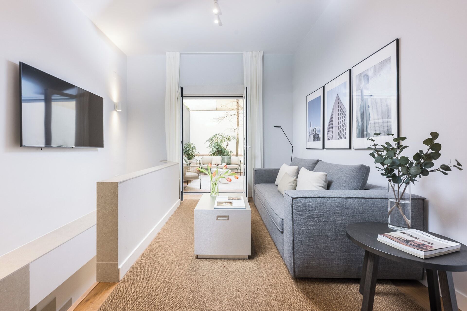 Una sala de estar moderna con un sofá gris, una mesa de centro y un televisor montado en la pared.