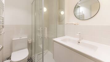 A bathroom with a toilet, a glass-enclosed shower, a sink, and a mirror.