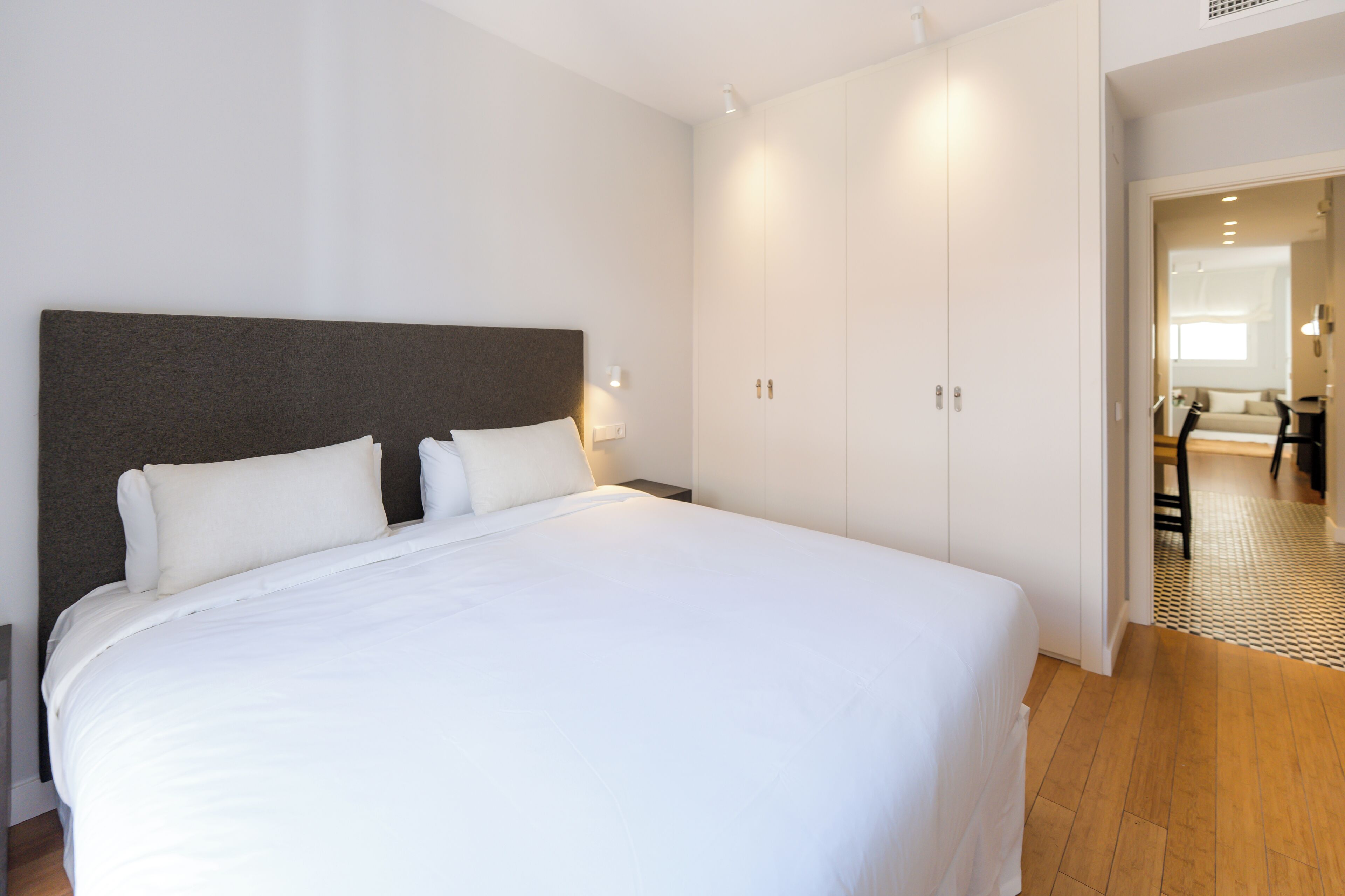 A neatly made bed with white linens, a dark headboard, and a white wardrobe with a mirror.