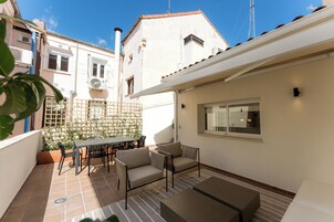 A patio with a table and chairs, a small garden, and a building with a tiled roof.