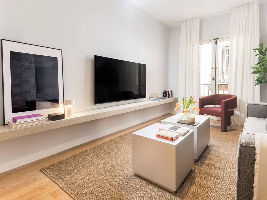 Un salón moderno con televisor de pantalla plana, una mesa de centro blanca, un sillón rojo y un sofá gris.