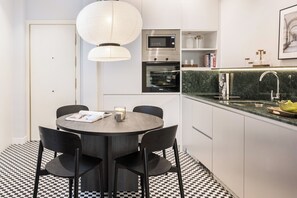 Una cocina moderna con comedor, que incluye una mesa redonda, sillas, una lámpara colgante, electrodomésticos integrados y un suelo a cuadros.