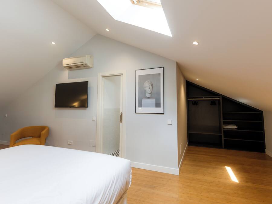 Een slaapkamer met een bed, een stoel, een televisie, een ingelijste foto, een kast en een dakraam.