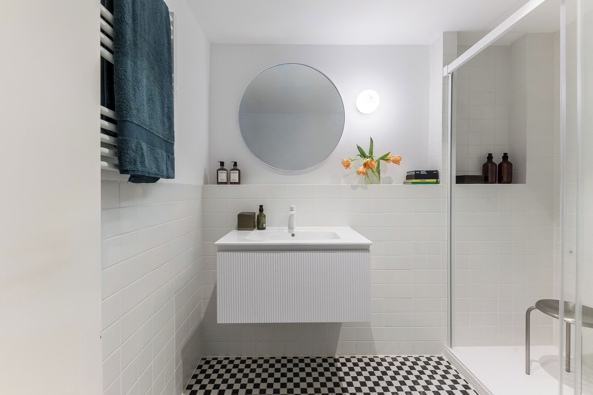 Un bany amb un lavabo blanc, un mirall rodó, un penjallinus i un sòl a escacs.