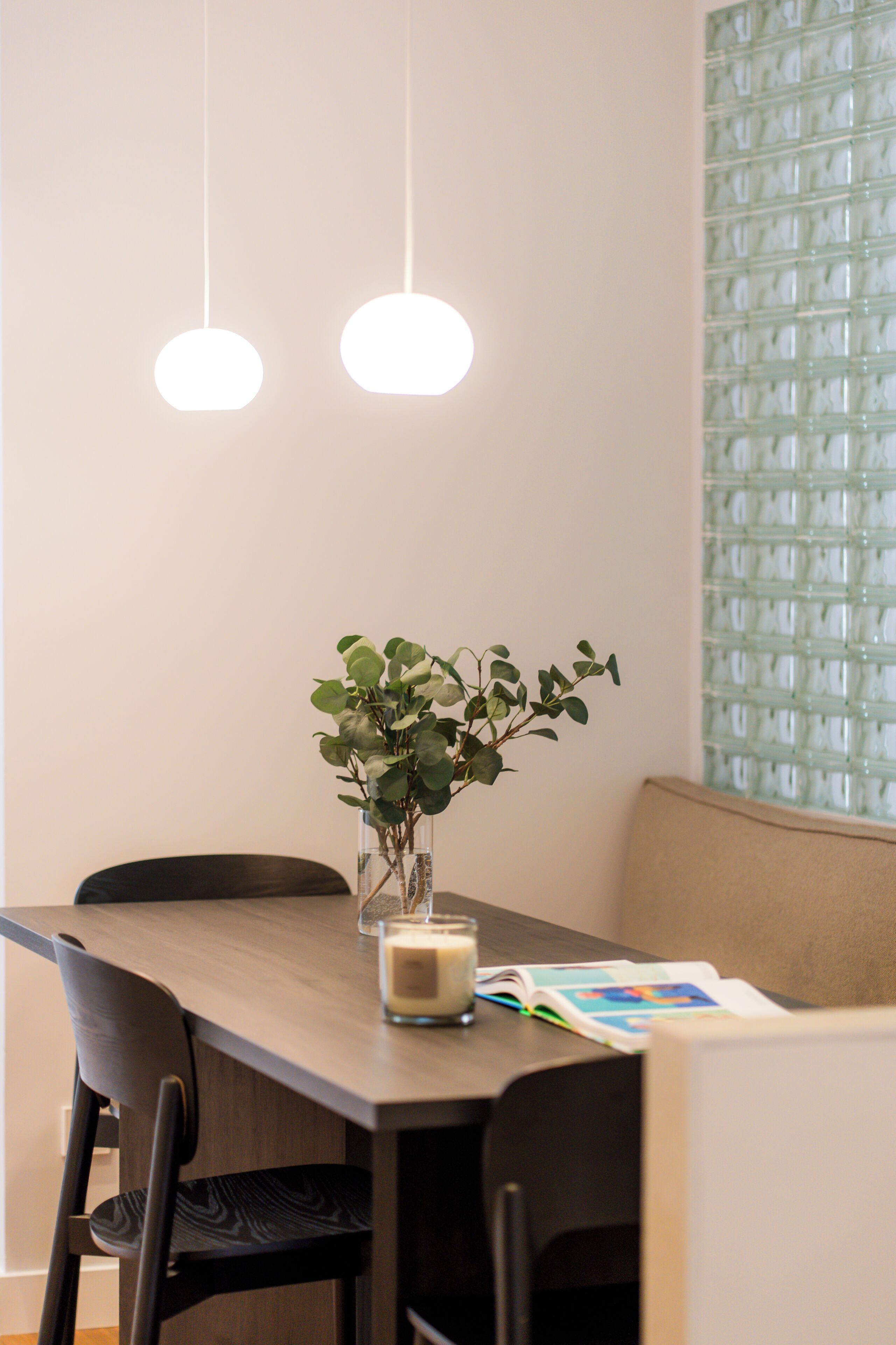Een eethoek met een tafel, stoelen, een vaas met groen en hangende lampen.