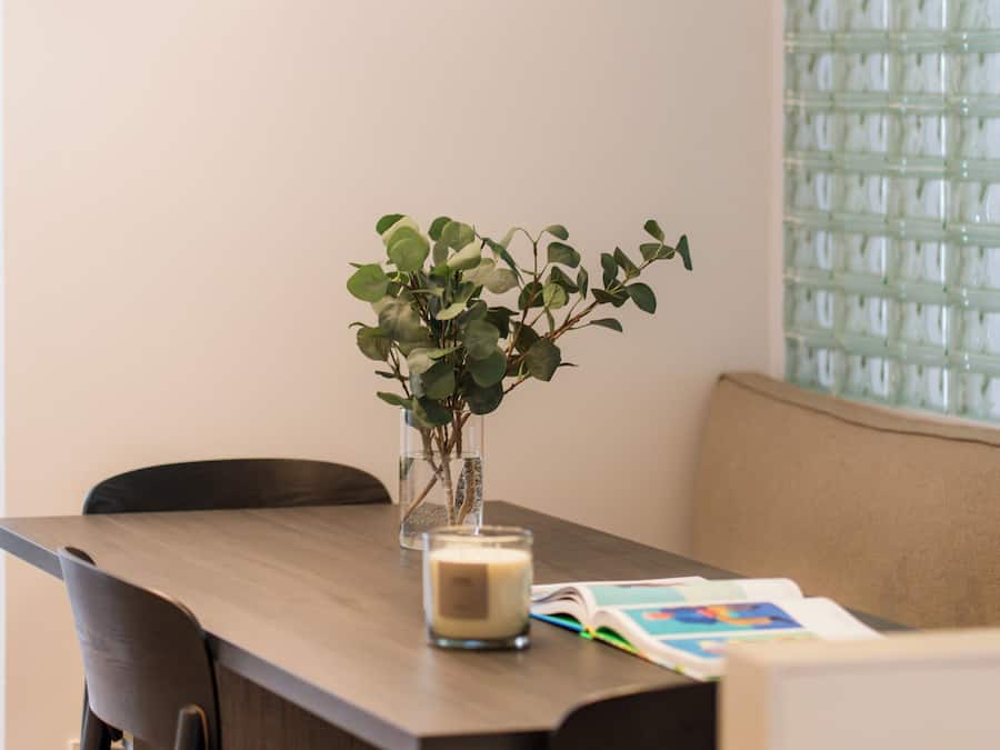 Een eethoek met een tafel, stoelen, een vaas met groen en hangende lampen.