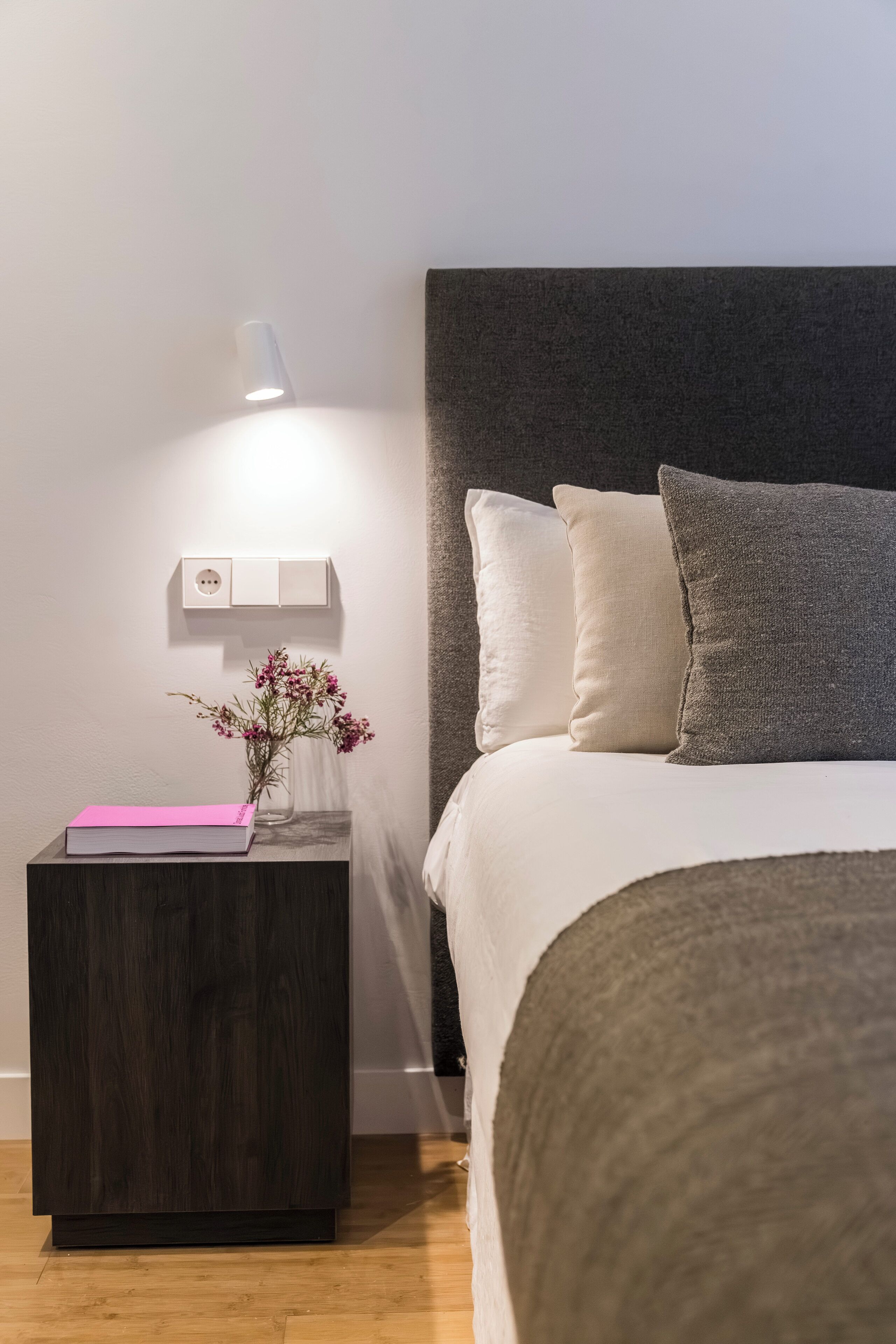 Un dormitorio ordenado con cama, mesita de noche y lámpara de pared.