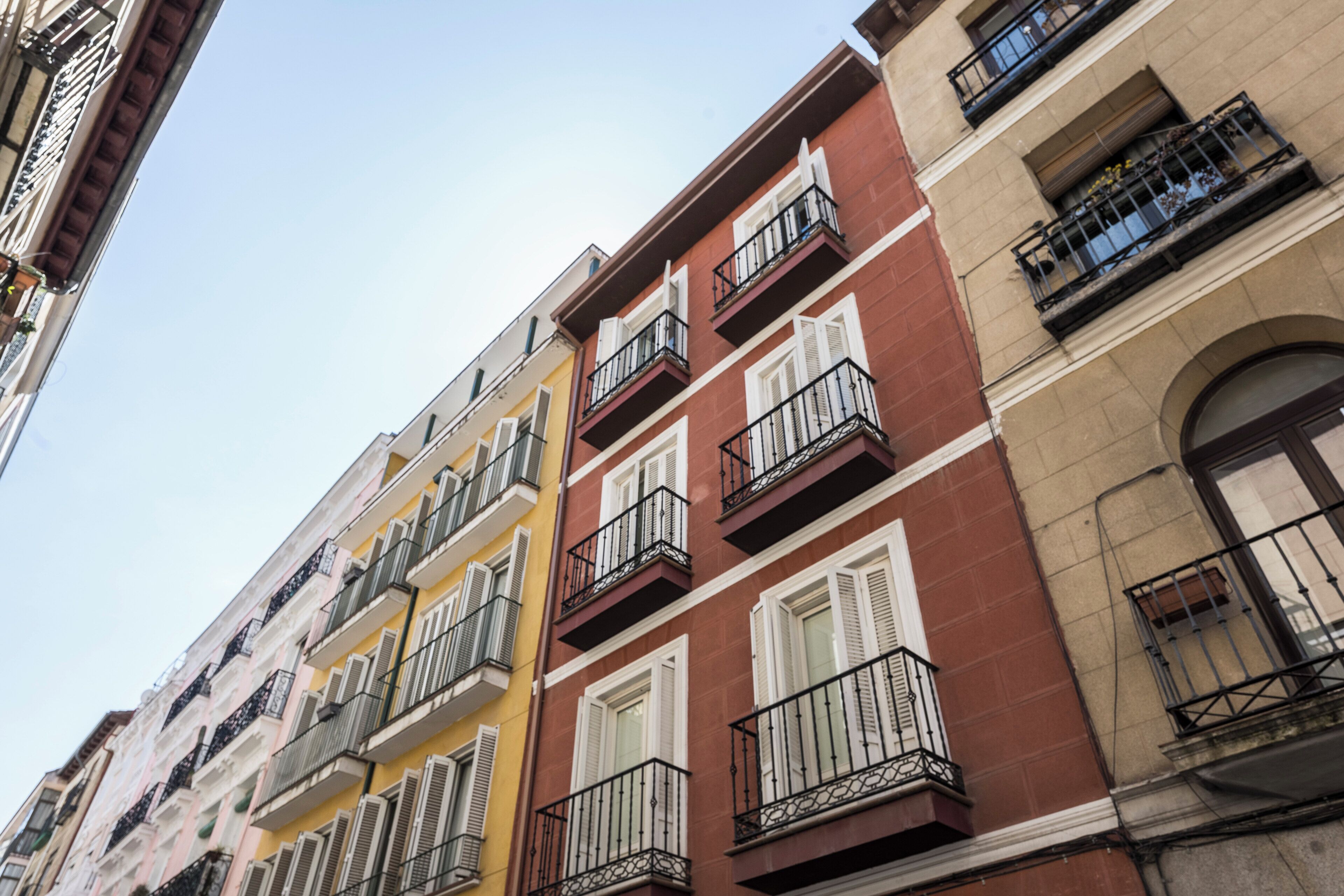 A multi-story building with balconies, windows with shutters, and a clear sky.