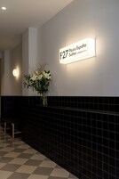Zona de recepción de un hotel, con un letrero que indica 'F27 Plaza España Suites' y un jarrón con flores en la pared.