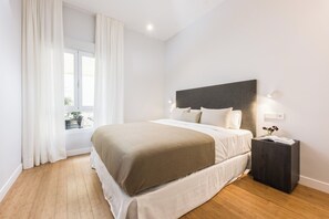 Ein modernes Schlafzimmer mit einem großen Bett, einem Nachttisch, einem Fenster mit Vorhängen und Blick ins Freie.