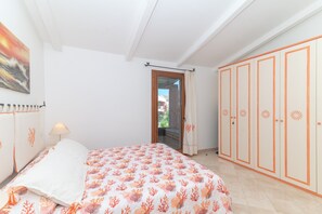Une chambre à coucher comprenant un lit, une table de chevet, une armoire et une porte donnant sur un balcon.