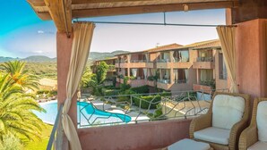 Ein Balkon mit Korbmöbeln, ein Pool und Blick auf ein Gebäude mit Balkonen.