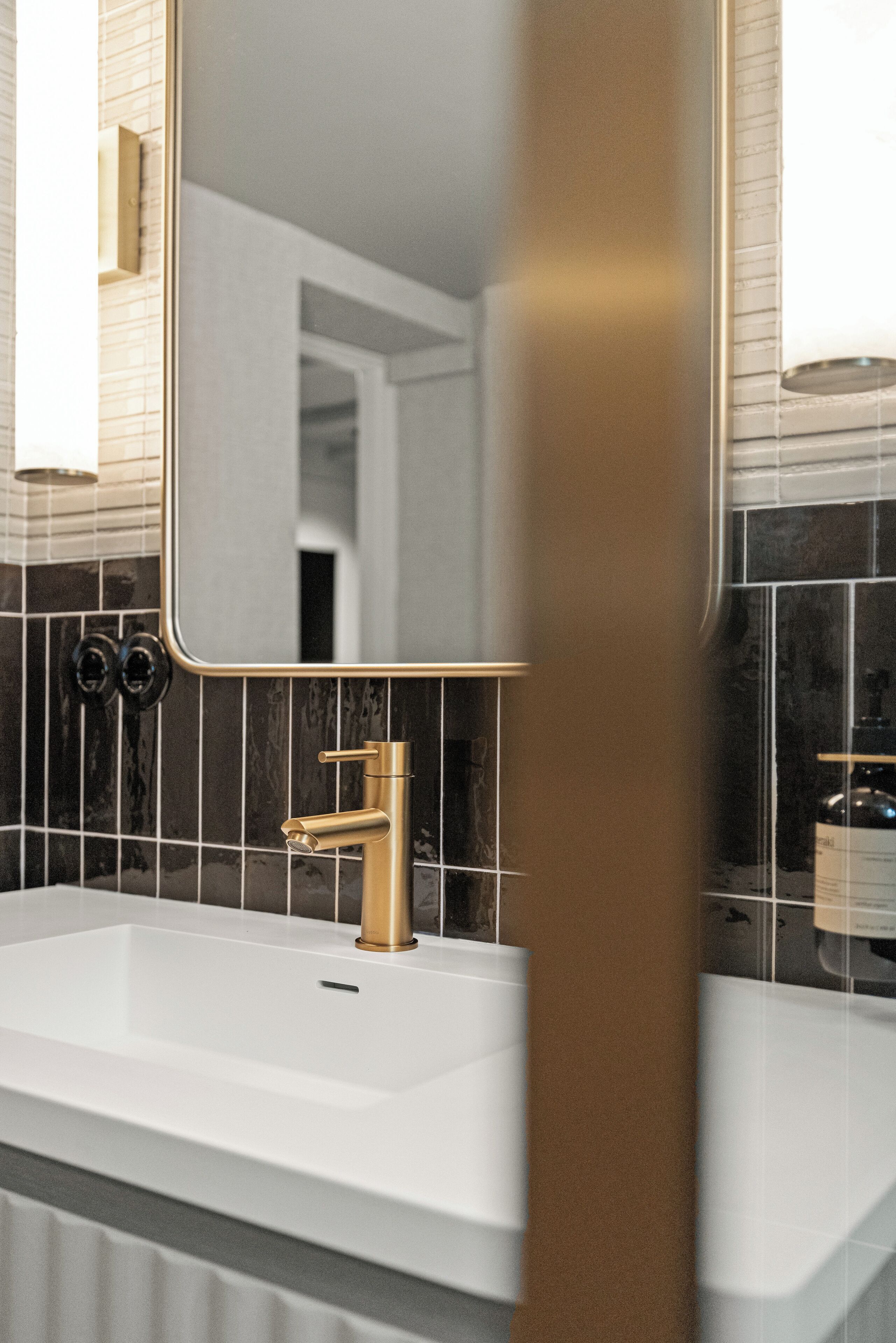 A bathroom with a white sink, gold faucet, and black and white tiled walls.