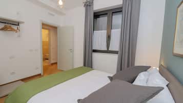 Una camera d'albergo con un letto, una finestra con tende, una porta e un lampadario.