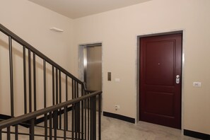A staircase with a metal railing leading to an elevator and a door with a number plate. - U Genova (Genoa)