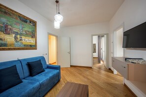 A modern living room with a blue sofa, a wooden coffee table, a painting on the wall, and a TV on a stand. - U Genova (Genoa)